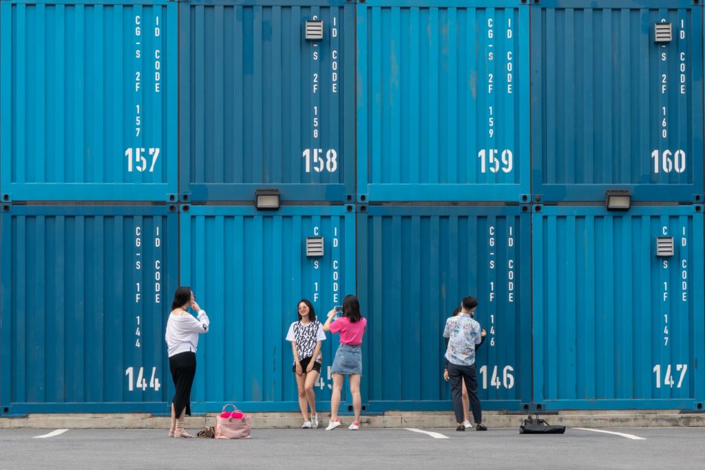 five women and man standing near shipping containers during daytime